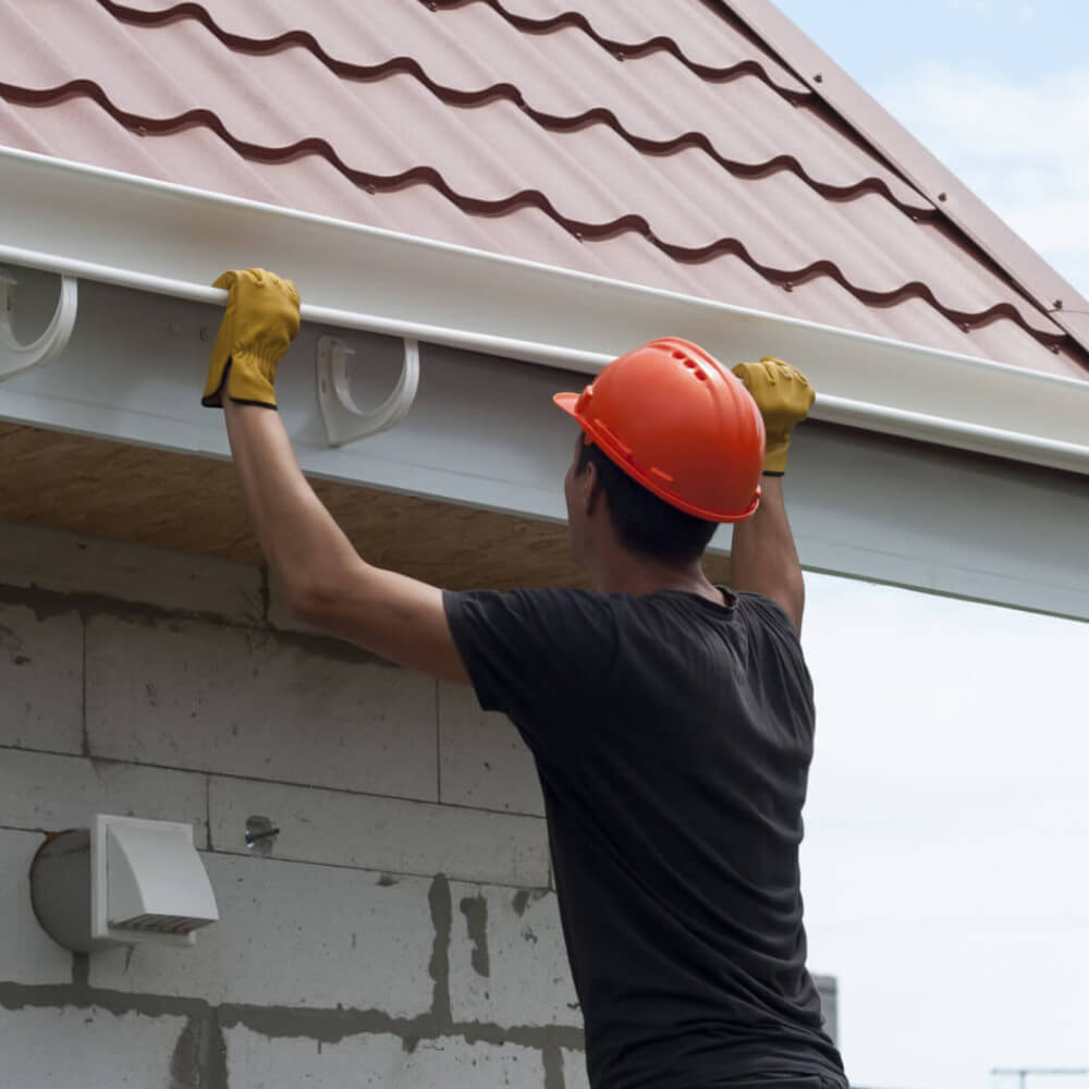 Picture demonstrating a McCoy Roofing's professional worker installing gutters on a home.