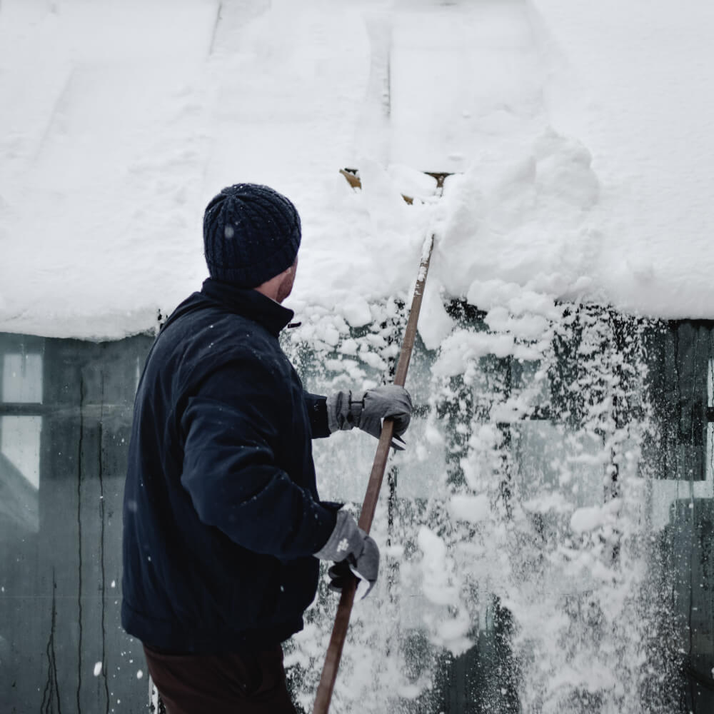 Homeowner safely removing snow from his roof to keep it in good shape.