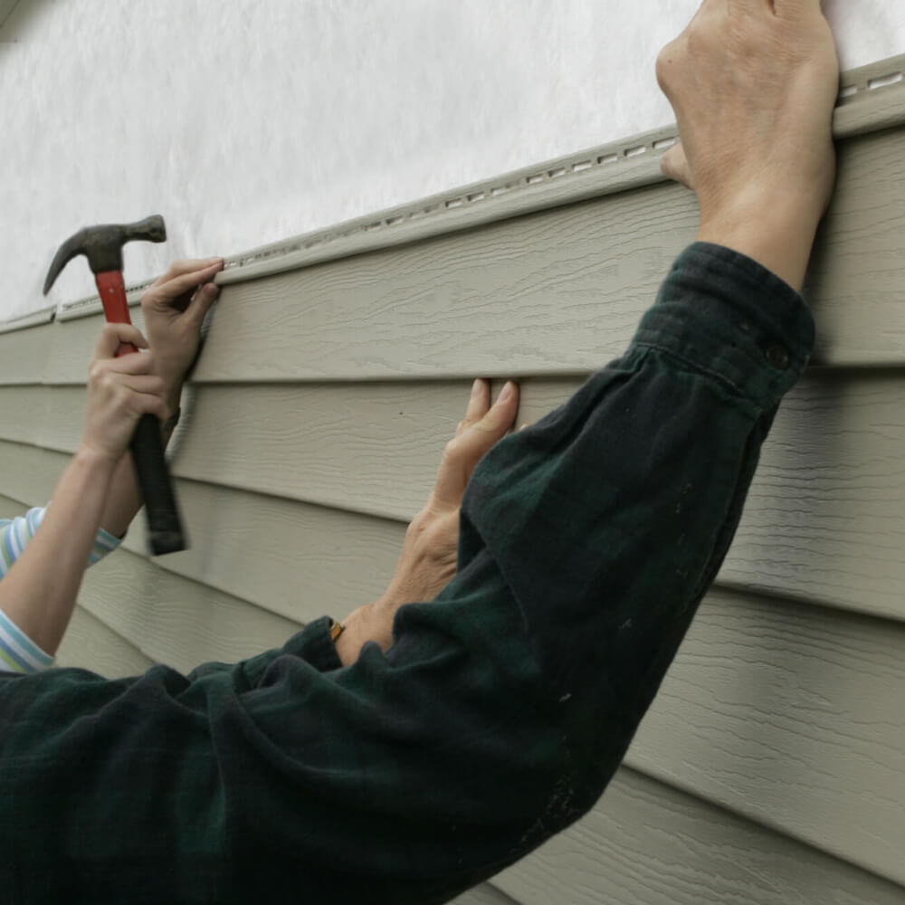 Picture of McCoy Roofing workers placing a vinyl siding on a home.